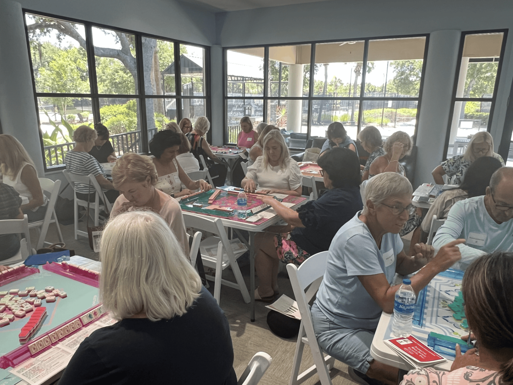 Players mid-game around teal and pink mahjong tables