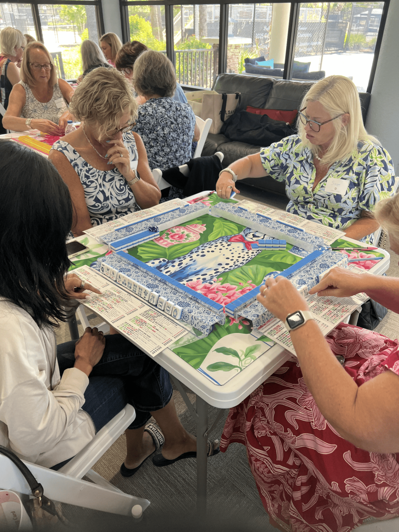 Players gathered around a blue floral mahjong table