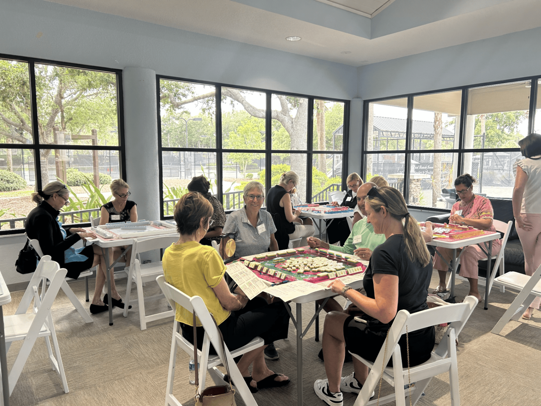 A sunlit room of mahjong tables in play
